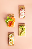 Crispbread with sour cream, cheese and tomatoes, radish, eggs, avocado on a pink paper background. Healthy concept copy space. Top view of Superfood protein toast with toppings. Polyunsaturated fat