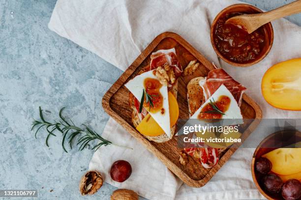 overhead view of two slices of toast with serrano ham, cheese, persimmon and chutney - serrano ham foto e immagini stock