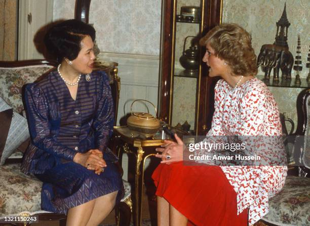 Diana, Princess of Wales, wearing a red and white patterned dress designed by Catherine Walker, speaks to Queen Sirikit of Thailand as she visits...