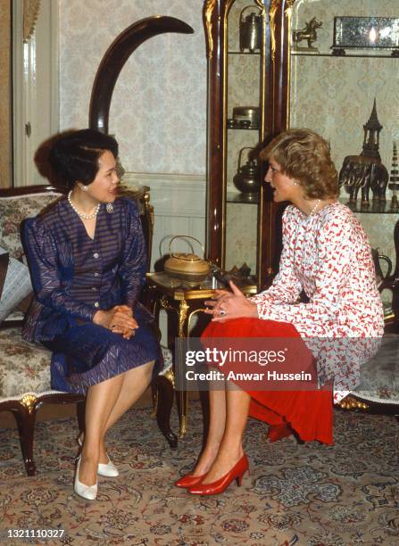 Diana, Princess of Wales, wearing a red and white patterned dress designed by Catherine Walker, speaks to Queen Sirikit of Thailand as she visits...