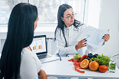Female nutritionist with laptop gives consultation to patient indoors in the office