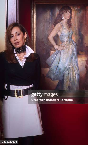 Daniela Zuccoli, wife of Italian TV presenter Mike Bongiorno, posing in her home next to a self-portrait of her. Milan , year 1996