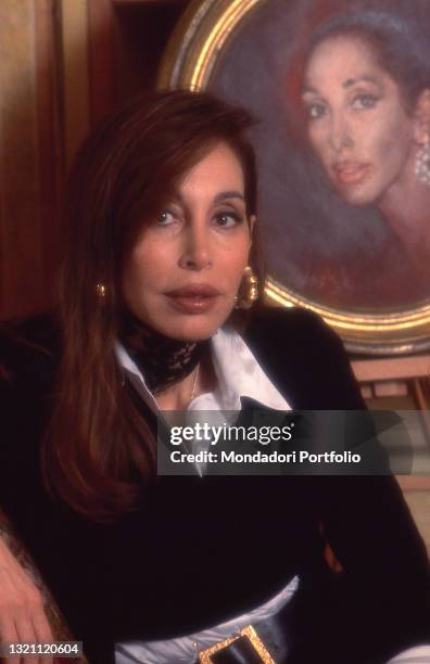 Daniela Zuccoli, wife of Italian TV presenter Mike Bongiorno, posing in her home next to a self-portrait of her. Milan , year 1996