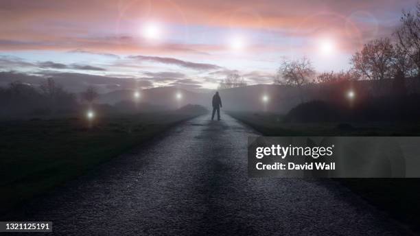 a ufo concept of glowing orbs, floating above a misty winters road just after sunset. with a silhouetted figure , back to camera, looking at the lights. - ufo abduction stock pictures, royalty-free photos & images