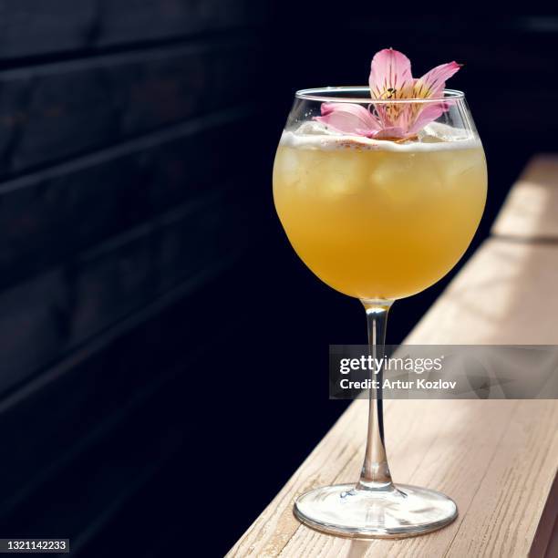 alcoholic drink. glass of yellow cocktail decorated with alstroemeria flower on wooden table against of black background. soft focus. copy space for text at left. romantic vacation concept - flouté photos et images de collection