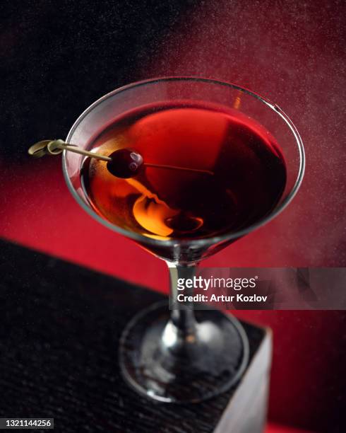 strong alcoholic cocktail or drink with cherry, backlit on dark red background surrounded by fine water spray. vertical format, soft focus - liqueur - fotografias e filmes do acervo
