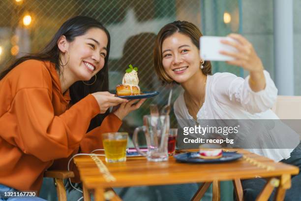 weibliche freunde genießen es, süßes essen im café zu essen und ihre zeit in sozialen medien zu teilen - asian restaurant stock-fotos und bilder