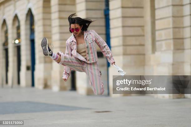 Alessandra Huynh wears a silver chain necklace, a pale yellow ribbed crop top, a rainbow striped Lee jacket with matching multicolor denim large...