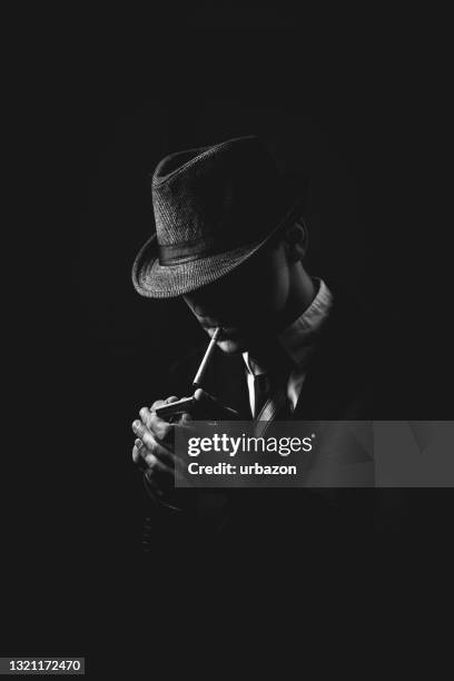 retro man in suit and hat lighting a cigarette - trilby stock pictures, royalty-free photos & images