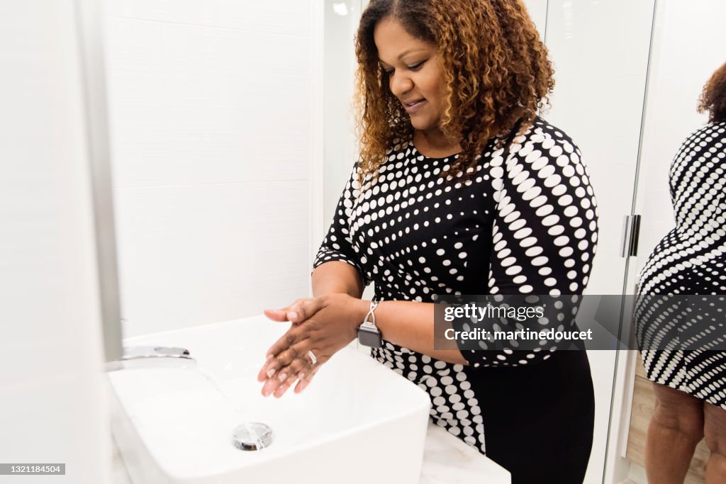 Mujer con cuerpo positivo que se lava las manos en el lavabo del baño.