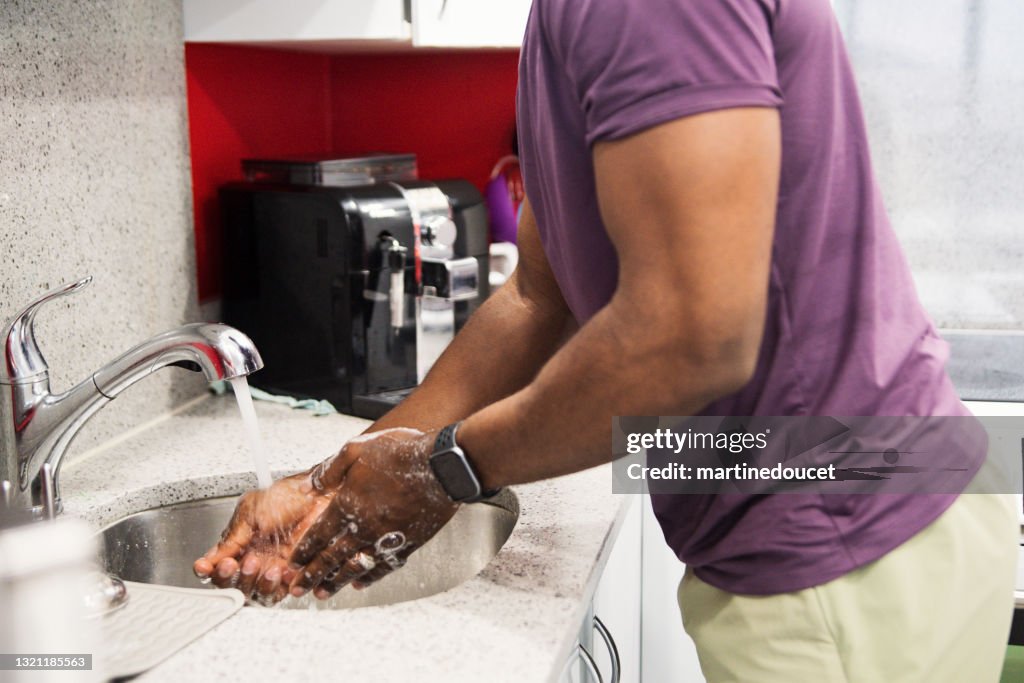 African-American man washing hands in kitchen sink.