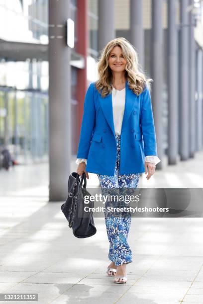 German TV host Frauke Ludowig wearing a blue blazer by Sem Per Lei, white pants with blue floral design by Sem Per Lei, a dark blue shopper bag with...