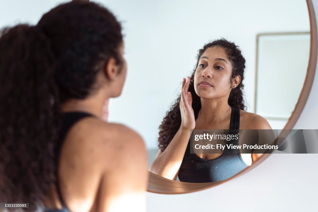 民族の女性は、円形の鏡を見ながら日焼け止めを適用します