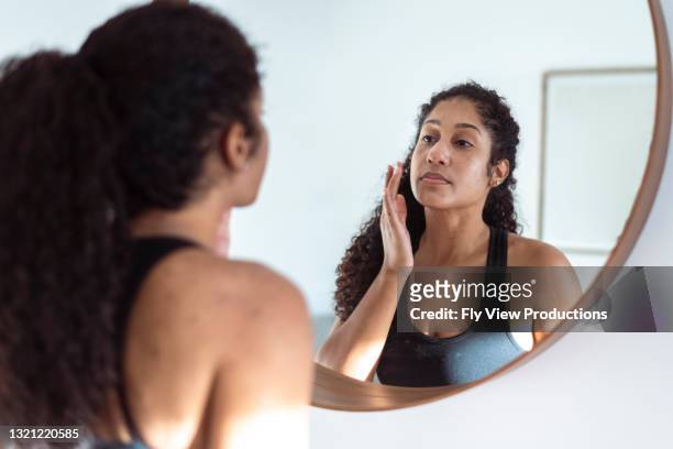 de etnische vrouw past zonnebrandcrème toe terwijl het kijken in cirkelvormspiegel - acne stockfoto's en -beelden