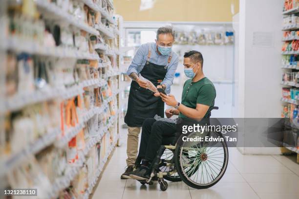 asiatische indische mann mit behinderung auf rollstuhl fragen senior mann einzelhandelsassistent auf seiner einkaufsliste von smartphone im supermarkt am wochenende - infolist stock-fotos und bilder