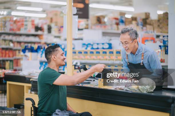 asian indian man with disability on wheelchair credit card purchase check out at cashier supermarket during weekend - online bank service stock pictures, royalty-free photos & images