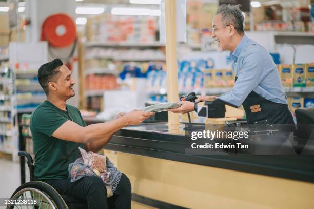 asiatische indische mann mit behinderung auf rollstuhl check-out in der kasse supermarkt am wochenende - markt verkaufsstätte stock-fotos und bilder