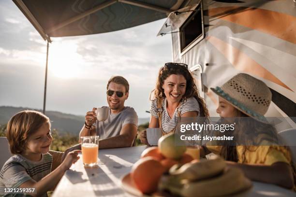 glückliche familie im gespräch am picknicktisch am wohnmobil-anhänger in der natur. - rvs stock-fotos und bilder