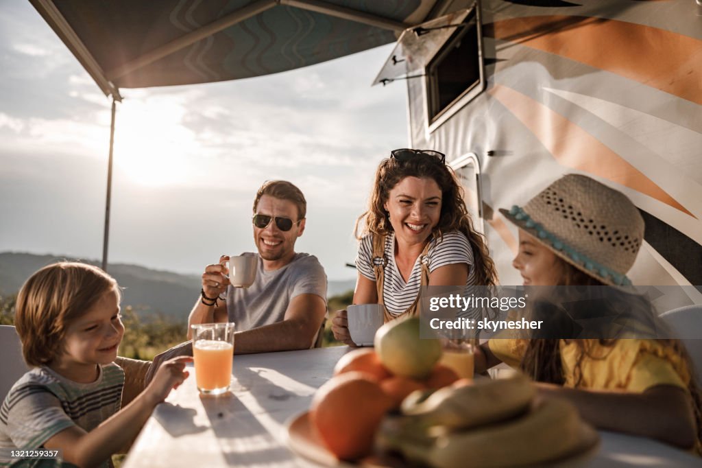 Happy family talking at picnic table by the camper trailer in nature.