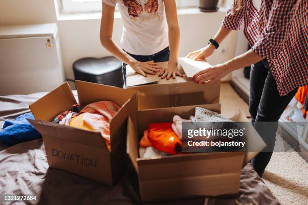 mother and daughter filling a boxes with clothes for donations - clothing donation stock pictures, royalty-free photos & images