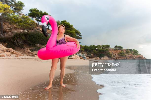 feliz mujer mayor en la playa con anillo de flamenco inflable - humour fotografías e imágenes de stock
