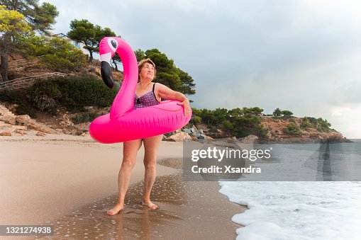 Happy senior woman on the beach with inflatable flamingo ring Happy senior woman on the beach with inflatable flamingo ring