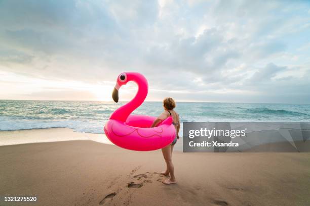 hogere vrouw op het strand met opblaasbare flamingo. actief gelukkig hoger concept. - alleen seniore vrouwen stockfoto's en -beelden