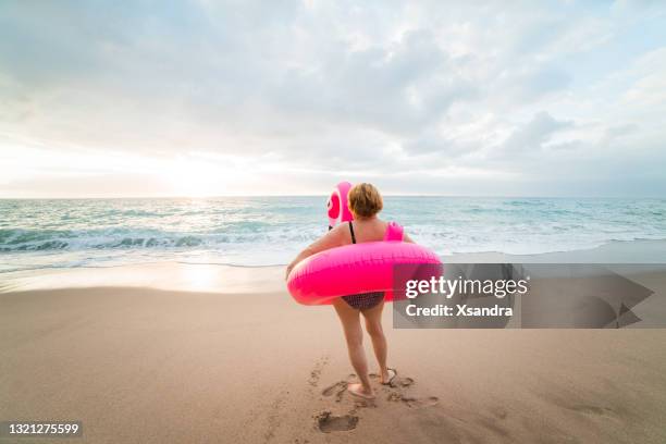 seniorin am strand mit aufblasbarem flamingo. aktives happy senior konzept. - coole oma stock-fotos und bilder