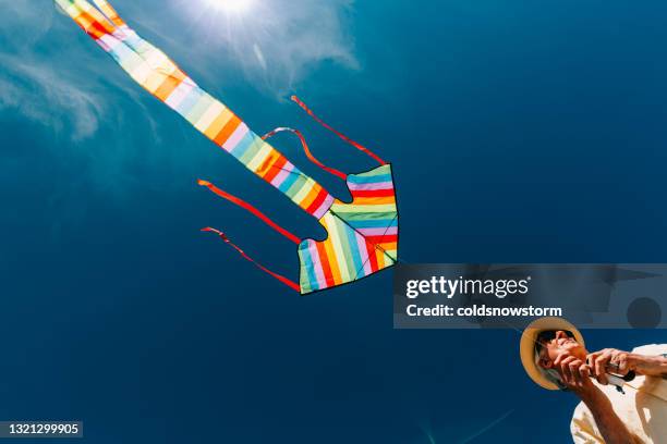 senior mann fliegen bunten regenbogen drachen am strand - kite toy stock-fotos und bilder