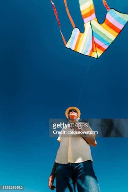 uomo anziano che vola aquilone arcobaleno colorato in spiaggia - kite toy foto e immagini stock