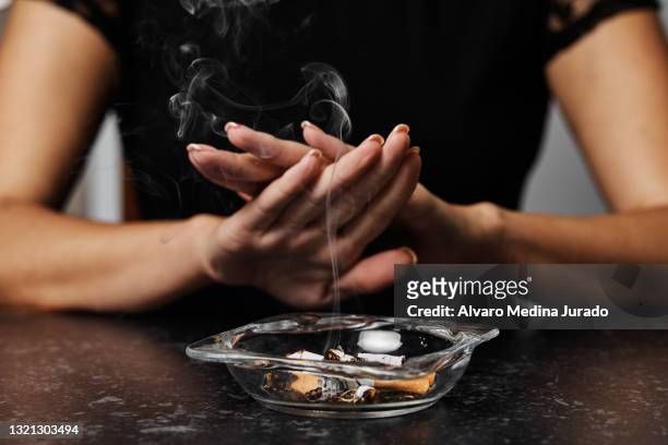 unrecognizable young woman refusing smoking with an ashtray full of cigarette butts in front of her. - ashtray stock pictures, royalty-free photos & images