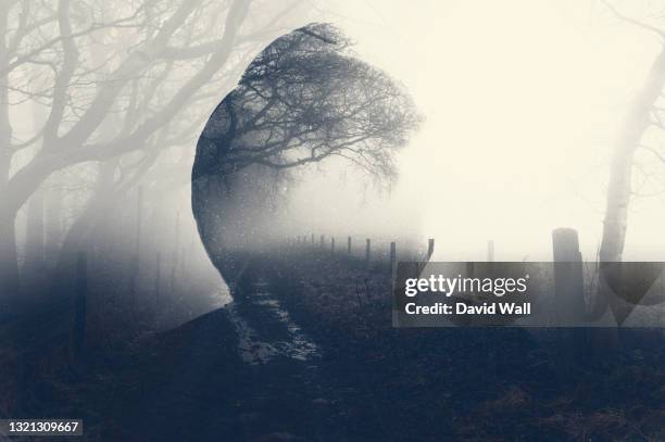 a double exposure of a spooky half transparent hooded figure. over layered over a foggy path in the countryside. on a moody foggy winters day. - missing person fotografías e imágenes de stock