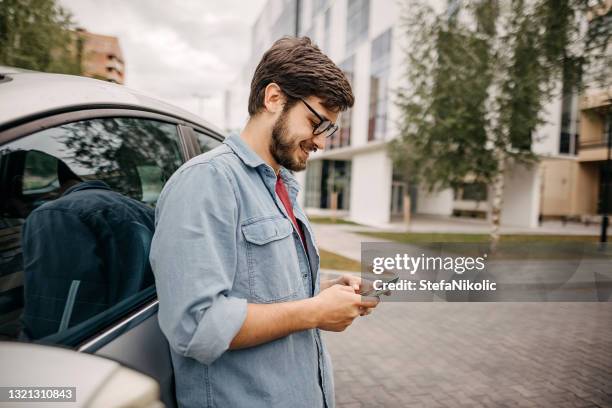 joven que usa el teléfono mientras espera a un amigo - carro fotografías e imágenes de stock