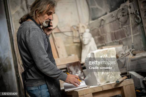 tailleur de pierre parlant au téléphone dans l’atelier - ouvrier maçon photos et images de collection