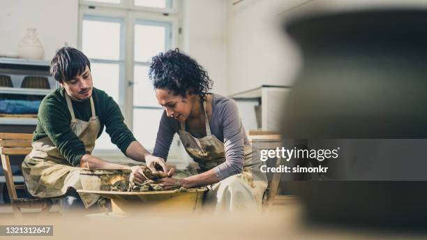 male potter teaching a female student how to centre the clay on the wheel - man wheel chair stock pictures, royalty-free photos & images