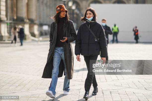 Model wears an orange embroideries pattern bob hat, a black wool turtleneck pullover, a black shiny leather crocodile pattern long coat, half blue...