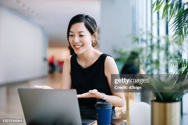 smiling professional young asian businesswoman talking in front of the camera having video conference with her business partners on laptop in a contemporary office space - laptop meeting fotografías e imágenes de stock