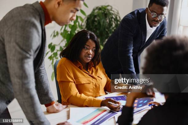 african american businesswoman sitting with her diverse team around a table in an office discussing work - big fat women stock pictures, royalty-free photos & images
