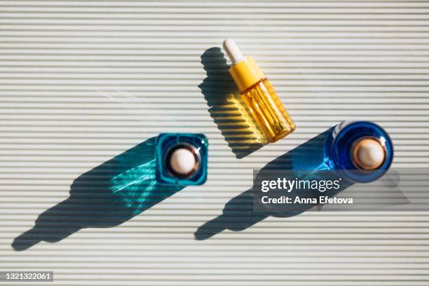 set of three glass vials on striped ultimate gray background. concept of skin care procedures for health and wellbeing. sunlight makes shadows and illuminating reflections from bottles. flat lay style. trendy colors of the year 2021 - argan oil stock pictures, royalty-free photos & images