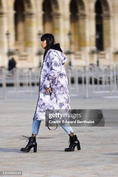 Model wears a black and white marble pattern long oversized puffer jacket, a black with yellow print hoodie sweater, blue faded denim ripped...