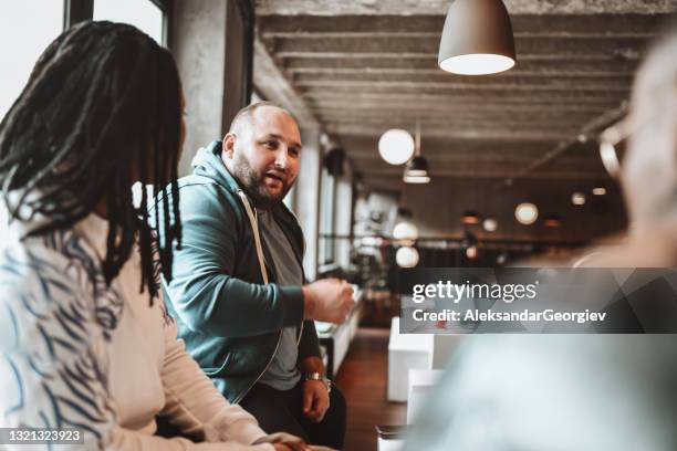 overweight balding male talking to african friends while enjoying coffee together - fat man stock pictures, royalty-free photos & images