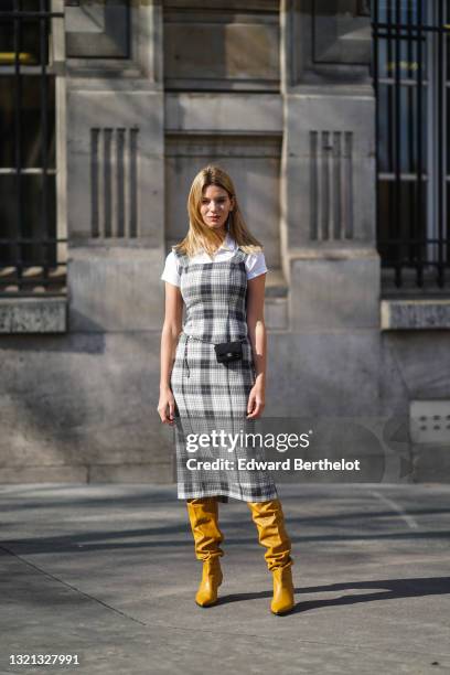 Natalia Verza @mascarada.paris wears silver earrings, a white polo shirt, a black and white checkered long tank top dress, a black fabric Chanel belt...
