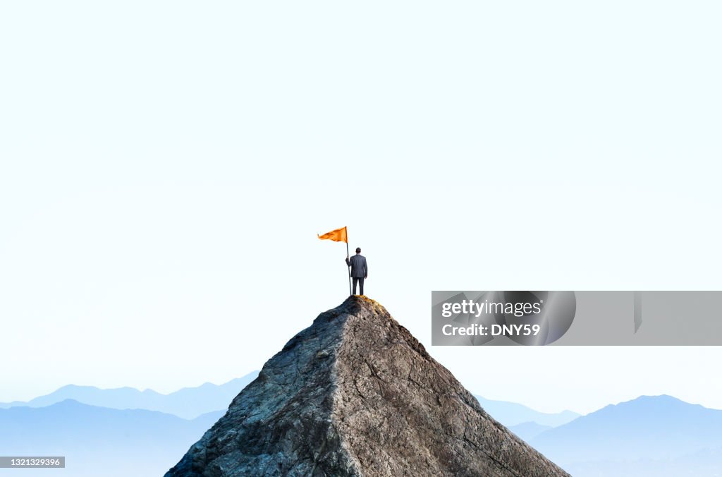 Uomo d'affari in cima alla vetta della montagna detiene una grande bandiera