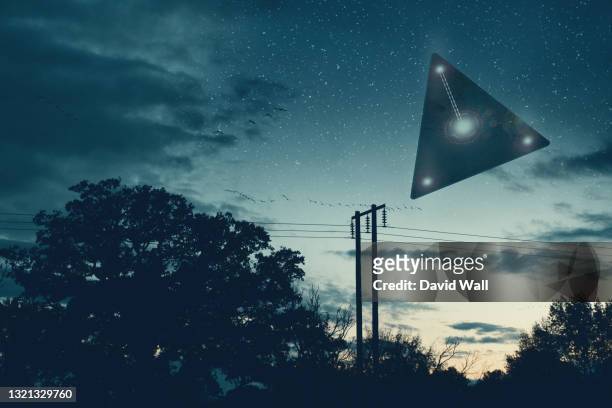 ufo concept. a flying triangle floating above the countryside at night. - flying saucer fotografías e imágenes de stock