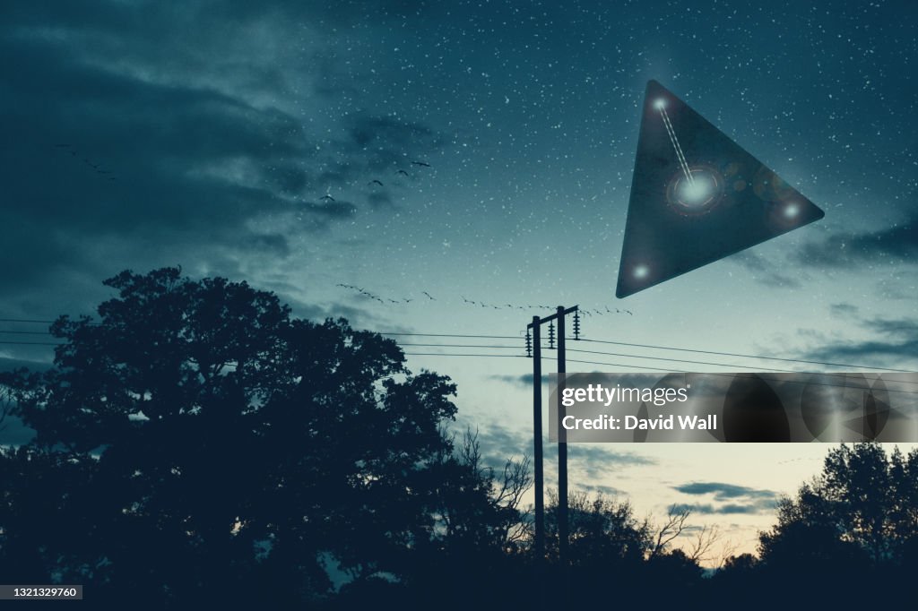 UFO concept. A flying triangle floating above the countryside at night.