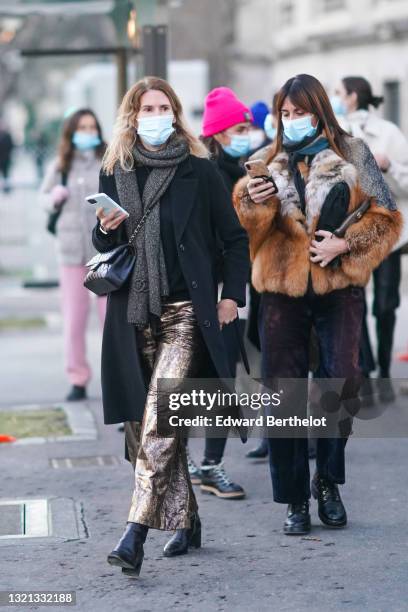 Guest wears a dark gray Chanel scarf, a black pullover, a black long coat, a black shiny leather Chanel Timeless crossbody bag, gold shiny pants,...