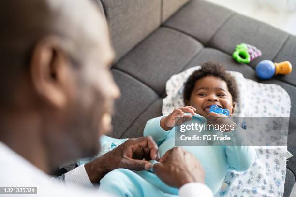 father playing with baby son and changing his clothes at home - nappy change imagens e fotografias de stock