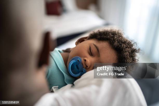 vater legt kleinen sohn zu hause auf den armen schlafen - african american dad stock-fotos und bilder