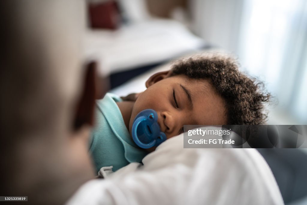 Pai colocando filho bebê para dormir em seus braços em casa