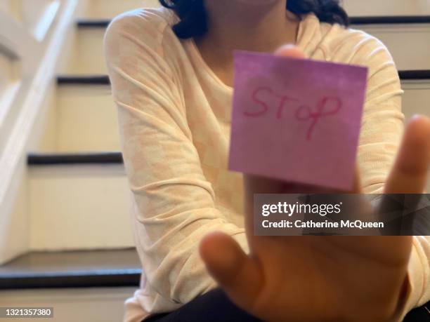 unrecognizable mixed-race teen girl holds up note with the word “stop” - fake news stock-fotos und bilder